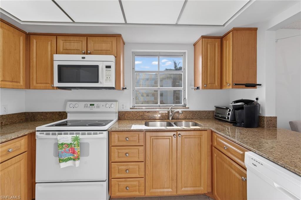 Kitchen featuring white appliances, light stone countertops, and brown cabinets