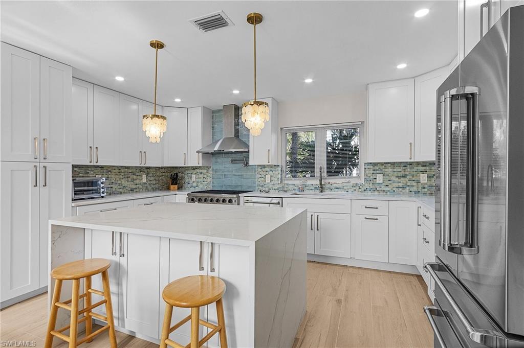 Kitchen featuring freestanding refrigerator, light stone counters, a kitchen bar, white cabinetry, and wall chimney range hood