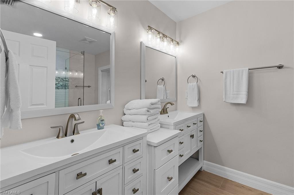 Bathroom featuring a shower stall, two vanities, and light wood finished floors