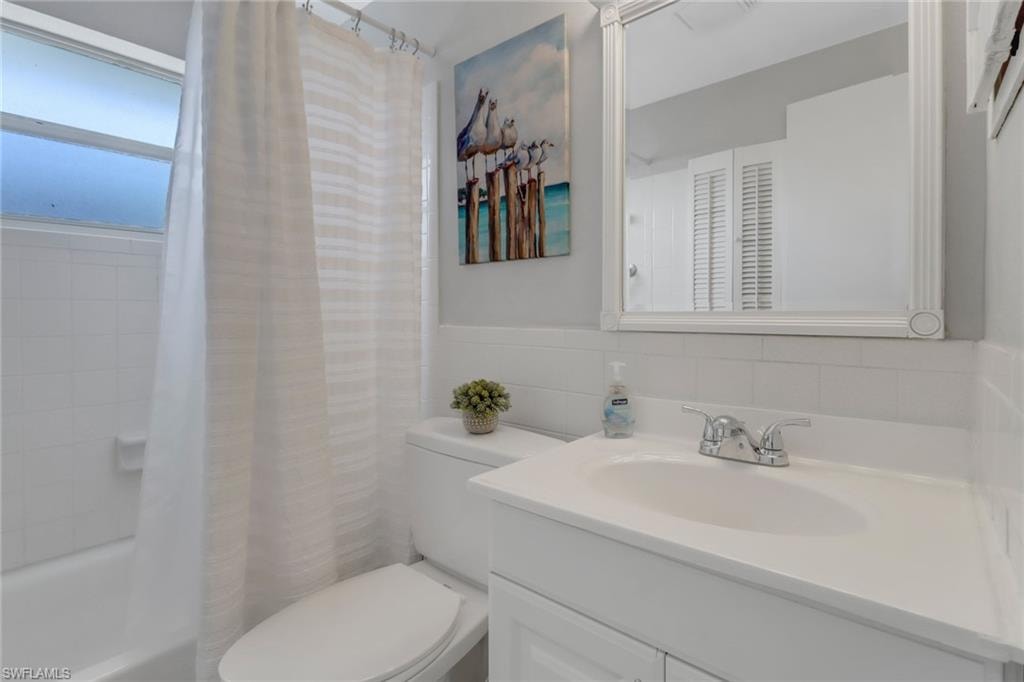 Full bathroom featuring tile walls, vanity, shower / bath combo, and toilet