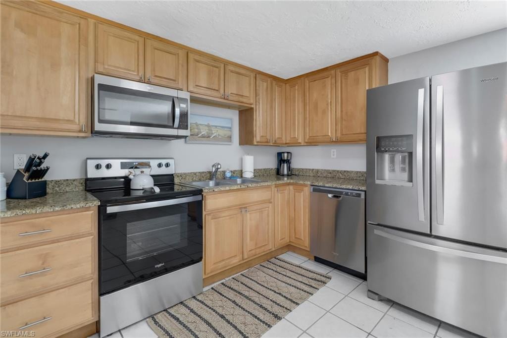 Kitchen featuring light stone countertops, stainless steel appliances, a textured ceiling, and sink