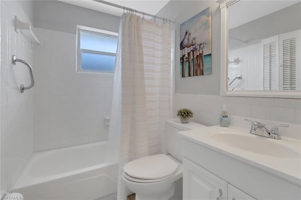 Full bathroom with tile walls, vanity, shower / tub combo with curtain, and toilet