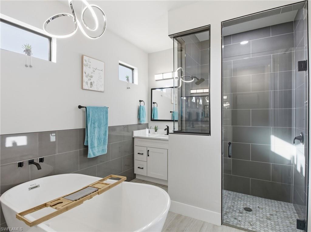 Full bath featuring a soaking tub, vanity, a shower stall, tile walls, and wainscoting