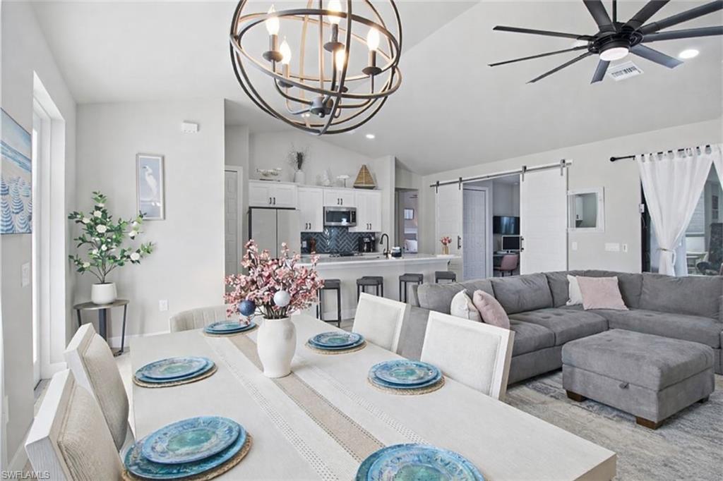 Dining area featuring a barn door, vaulted ceiling, ceiling fan, a chandelier, and recessed lighting