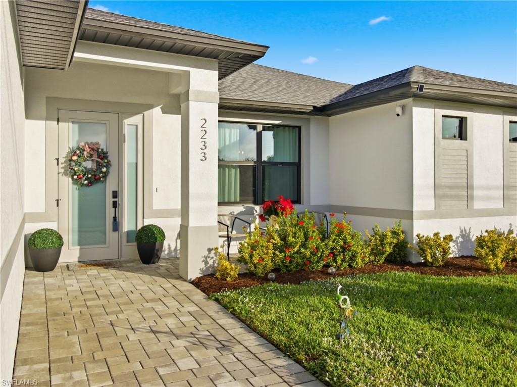 View of exterior entry featuring roof with shingles, stucco siding, and a yard