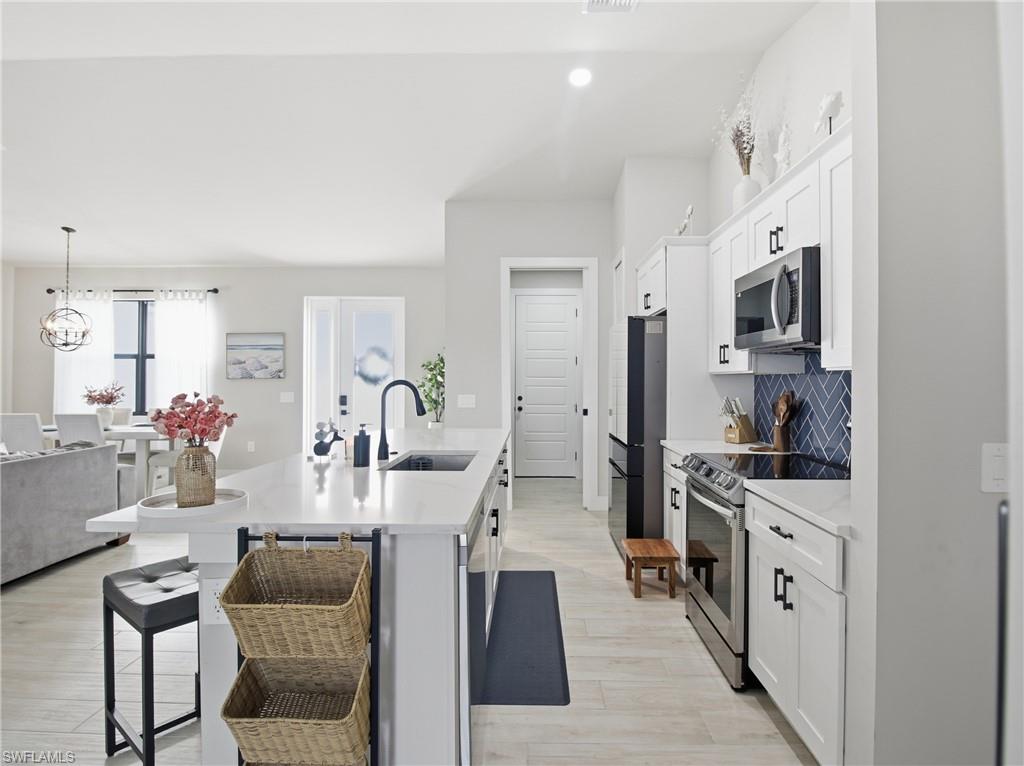 Kitchen featuring white cabinetry, an island with sink, a breakfast bar, appliances with stainless steel finishes, and pendant lighting