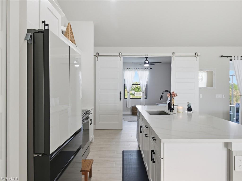 Kitchen featuring white cabinetry, freestanding refrigerator, light quartz countertops, an island with sink, and ceiling fan