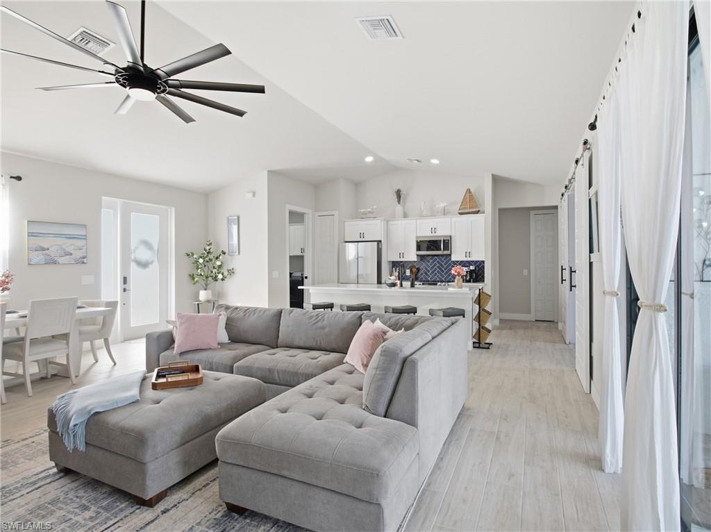 Living area with a barn door, vaulted ceiling, light flooring, and a ceiling fan