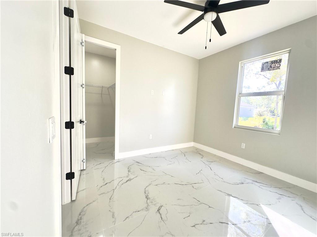 Unfurnished bedroom featuring light marble finish flooring, a walk in closet, and ceiling fan