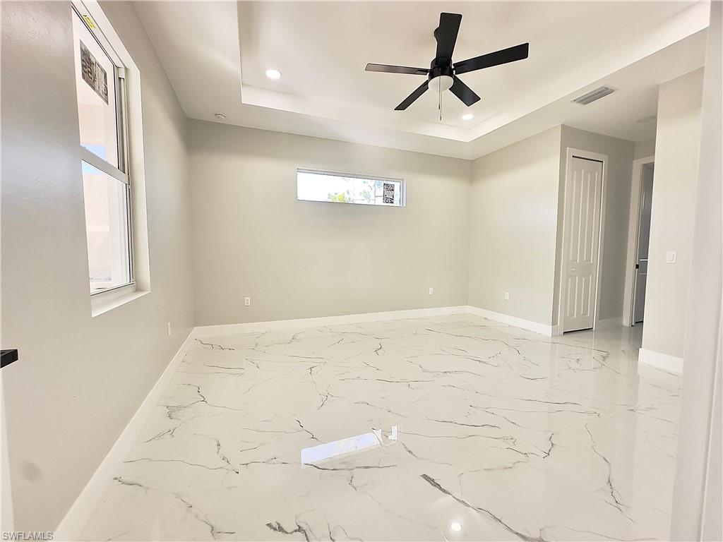 Empty room featuring light marble finish floors, recessed lighting, a tray ceiling, and a ceiling fan