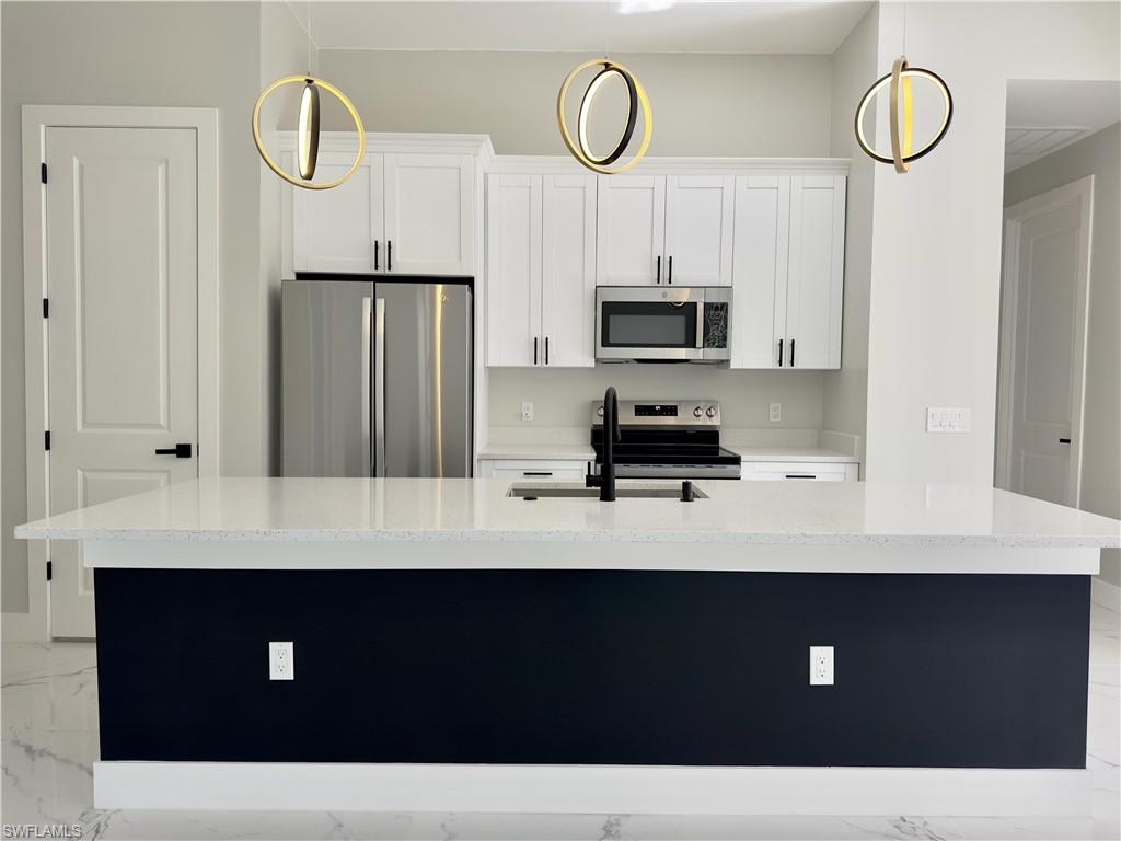 Kitchen with appliances with stainless steel finishes, white cabinets, light stone counters, and an island with sink