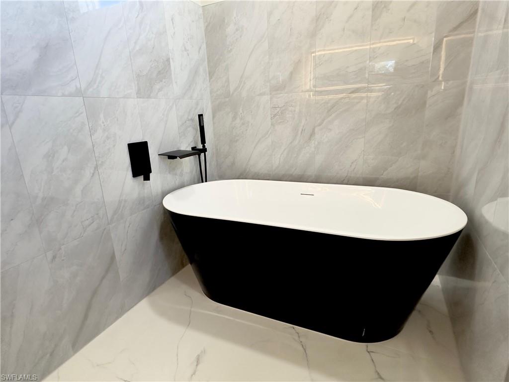 Bathroom with marble tiled floors, a freestanding bath, and tile walls