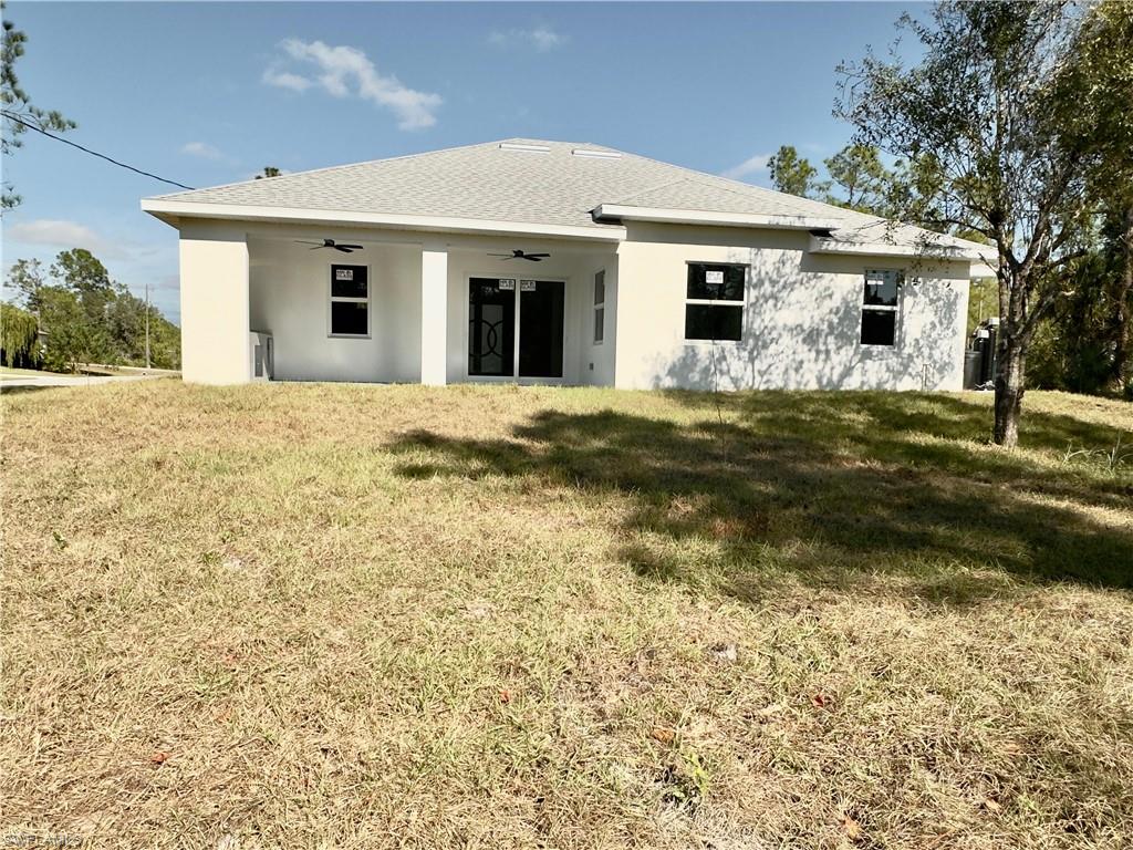 Rear view of property featuring a ceiling fan, a lawn, stucco siding, and a shingled roof