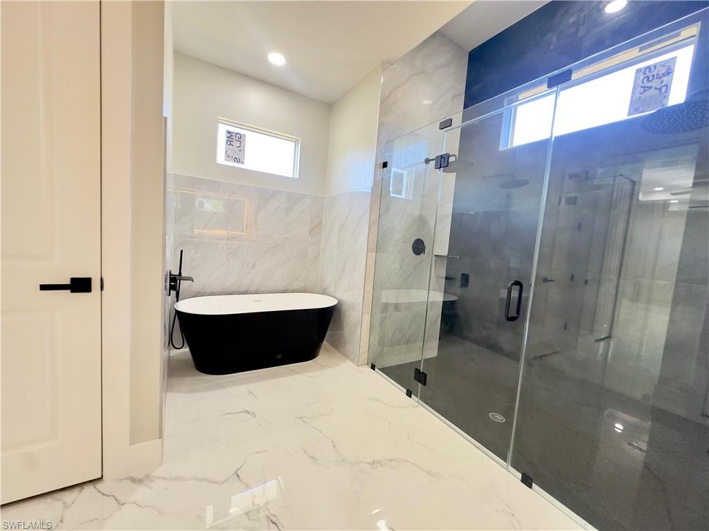 Bathroom featuring a soaking tub, healthy amount of natural light, a shower stall, marble tiled floors, and tile walls