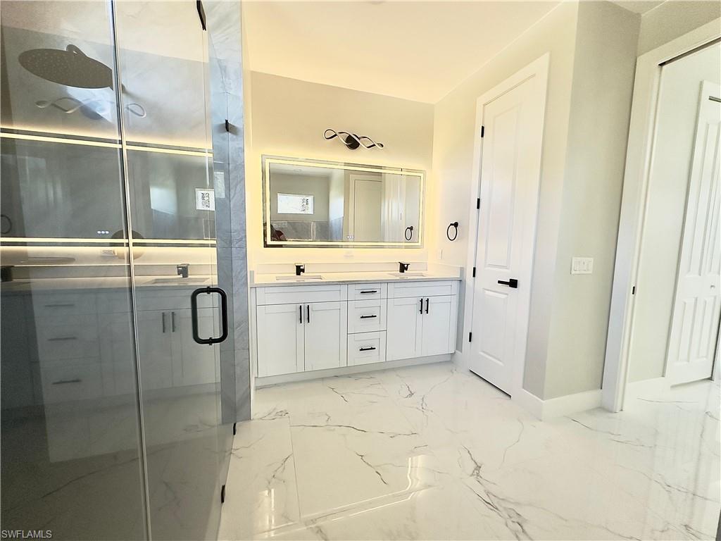 Bathroom with double vanity, light marble finish flooring, and a stall shower