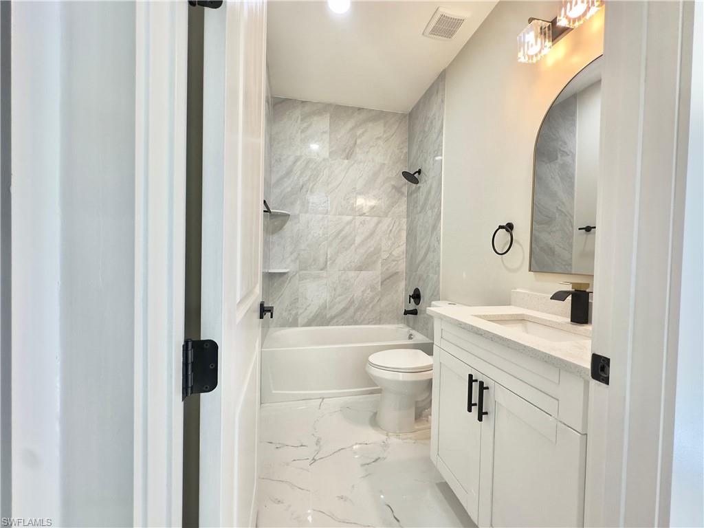 Bathroom featuring vanity, light marble finish flooring, and shower / washtub combination