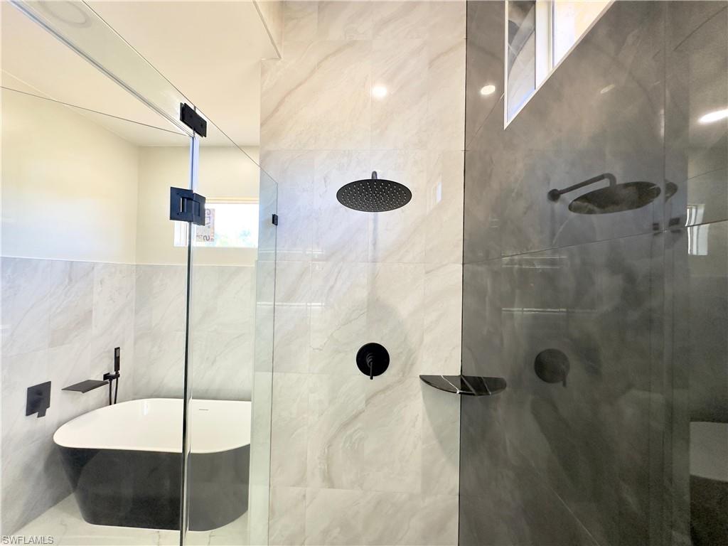 Bathroom featuring a soaking tub, a tile shower, and tile walls