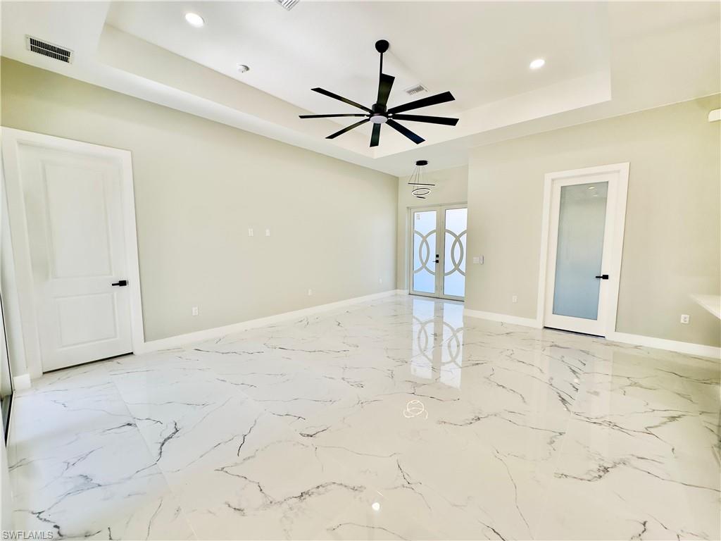 Unfurnished room featuring a tray ceiling, french doors, recessed lighting, light marble finish flooring, and ceiling fan