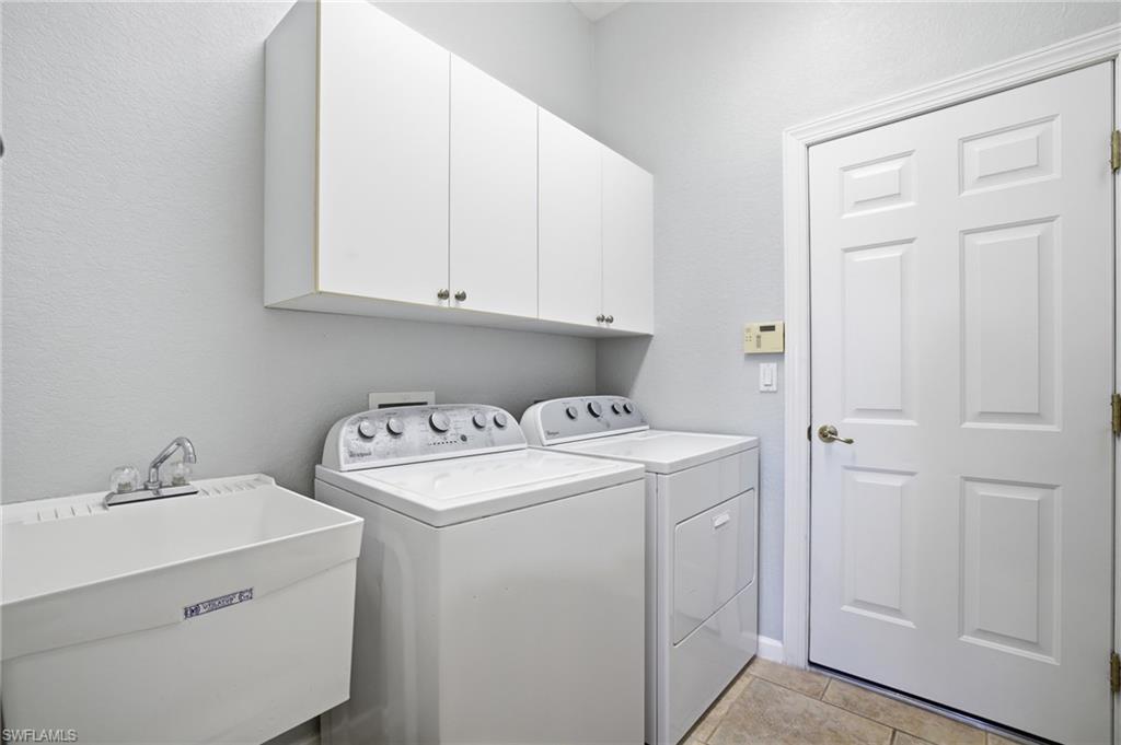 Washroom with cabinet space, washer and clothes dryer, light tile patterned flooring, and a textured wall