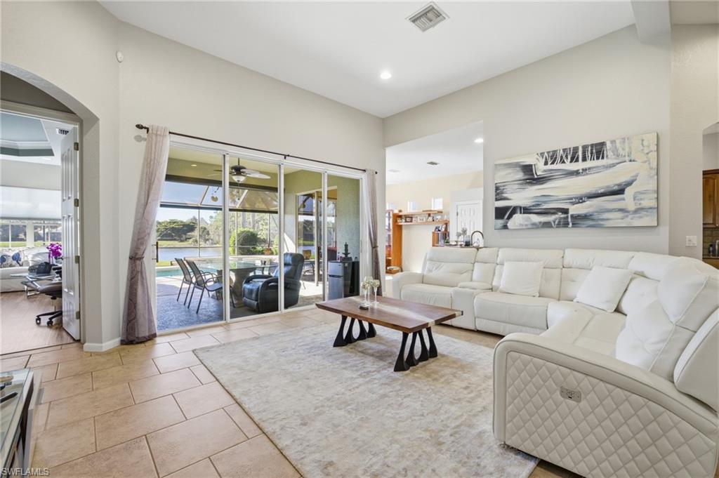 Living area with a sunroom, light tile patterned flooring, a water view, ceiling fan, and arched walkways