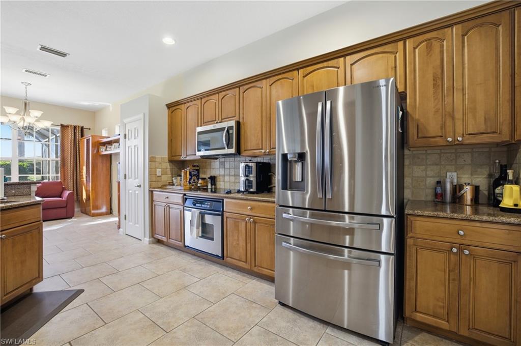 Kitchen featuring appliances with stainless steel finishes, brown cabinets, dark stone countertops, a chandelier, and hanging light fixtures