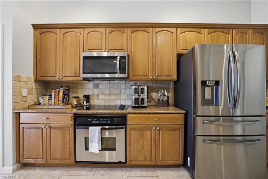 Kitchen featuring stainless steel appliances, brown cabinets, and light stone countertops
