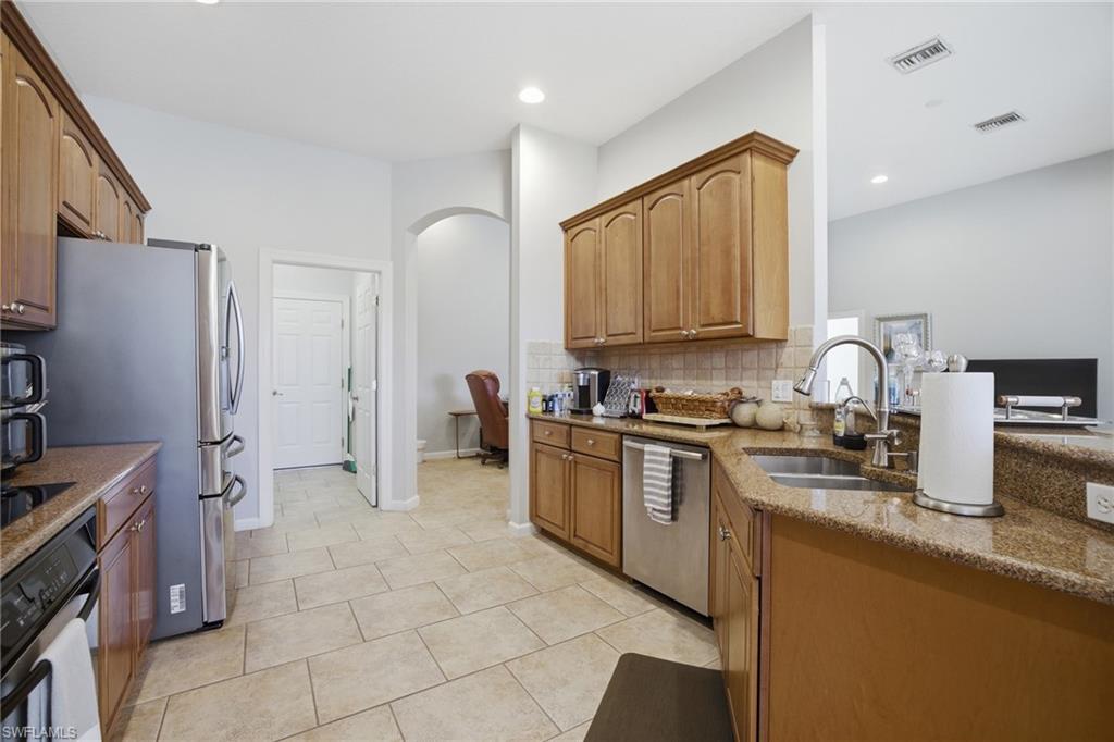 Kitchen with stainless steel appliances, dark stone countertops, arched walkways, backsplash, and light tile patterned floors