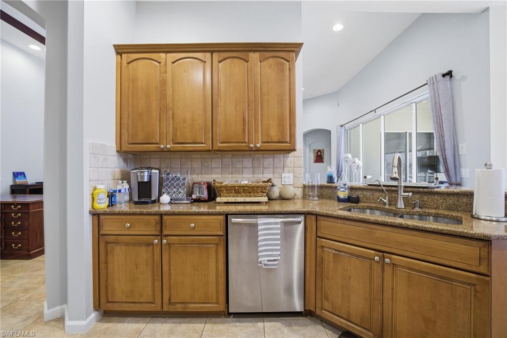 Kitchen with brown cabinetry, stainless steel dishwasher, light stone countertops, and recessed lighting