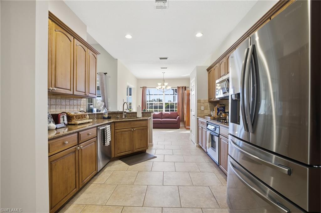 Kitchen featuring stainless steel appliances, a chandelier, dark stone countertops, tasteful backsplash, and hanging light fixtures