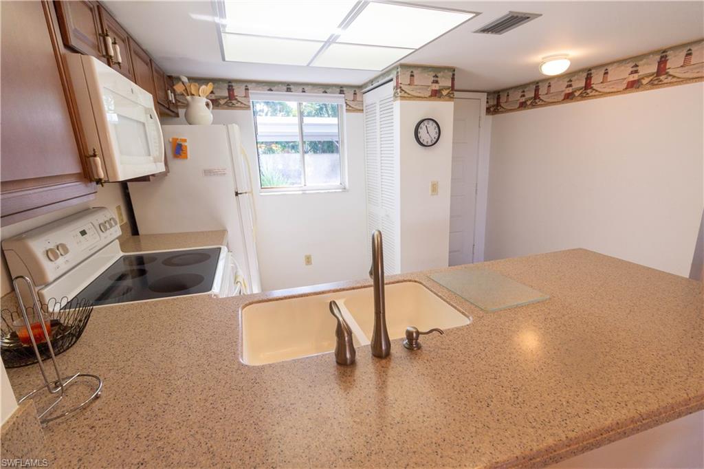 Kitchen featuring white appliances, light stone counters, a peninsula, and brown cabinets