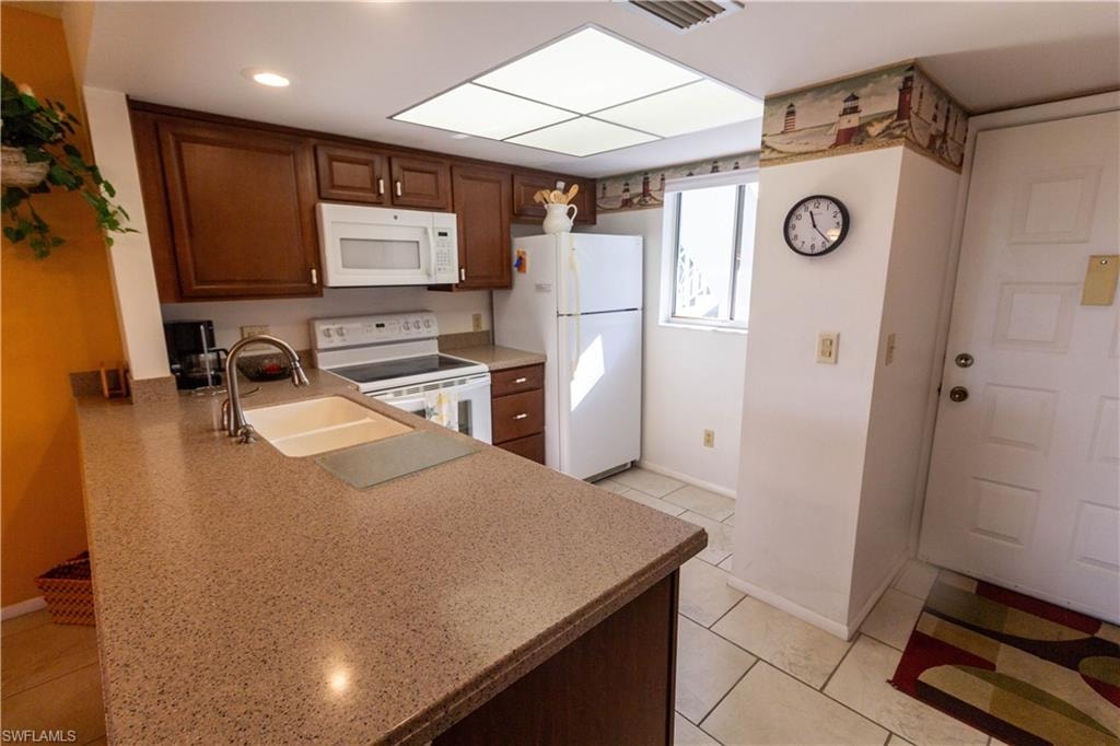 Kitchen with white appliances, light tile patterned floors, and a peninsula