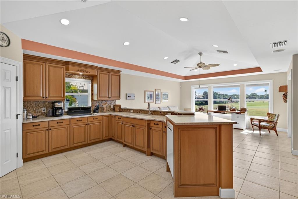 Kitchen with a tray ceiling, brown cabinetry, a peninsula, light tile patterned flooring, and decorative backsplash
