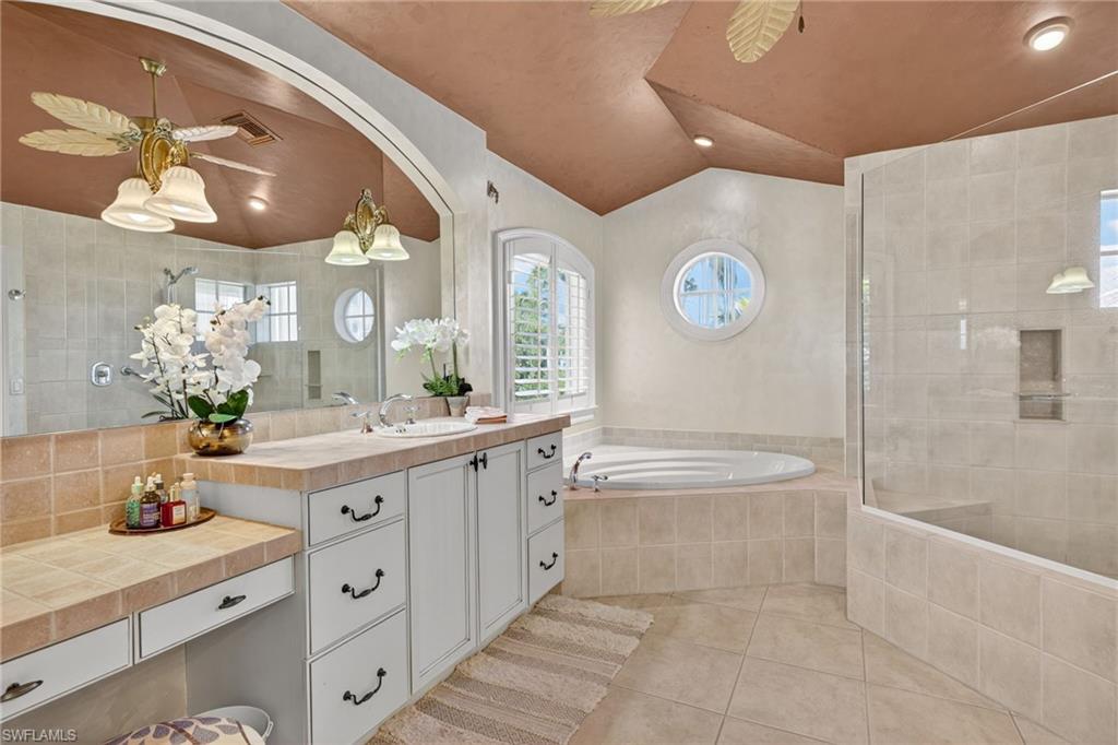Bathroom featuring ceiling fan, light tile patterned floors, vanity, a walk in shower, and vaulted ceiling