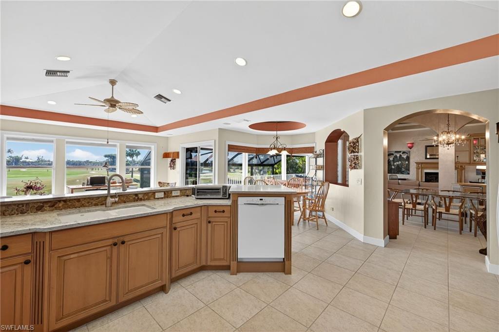 Kitchen with brown cabinets, a chandelier, white dishwasher, a tray ceiling, and light tile patterned floors