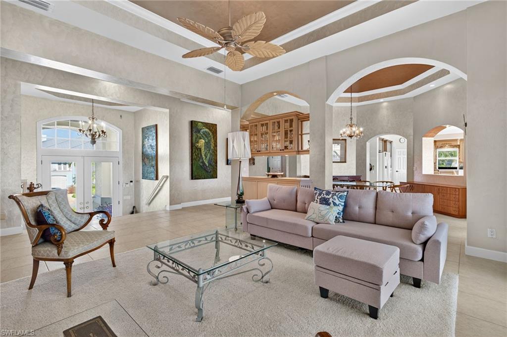 Living room with a raised ceiling, a chandelier, tile patterned floors, a high ceiling, and french doors