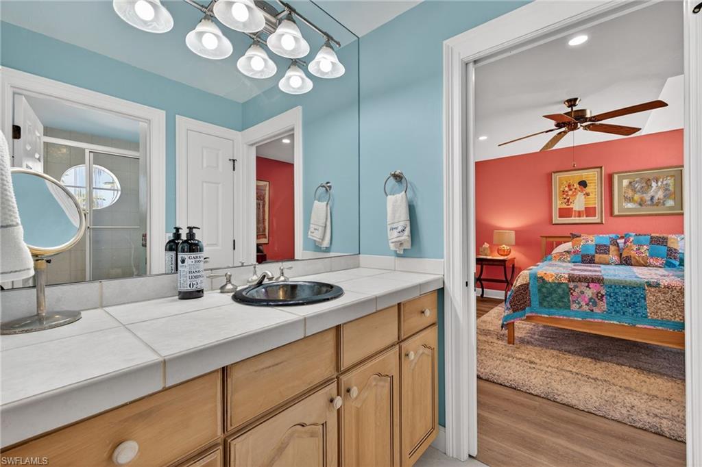 Full bath with light wood finished floors, vanity, a ceiling fan, a stall shower, and connected bathroom
