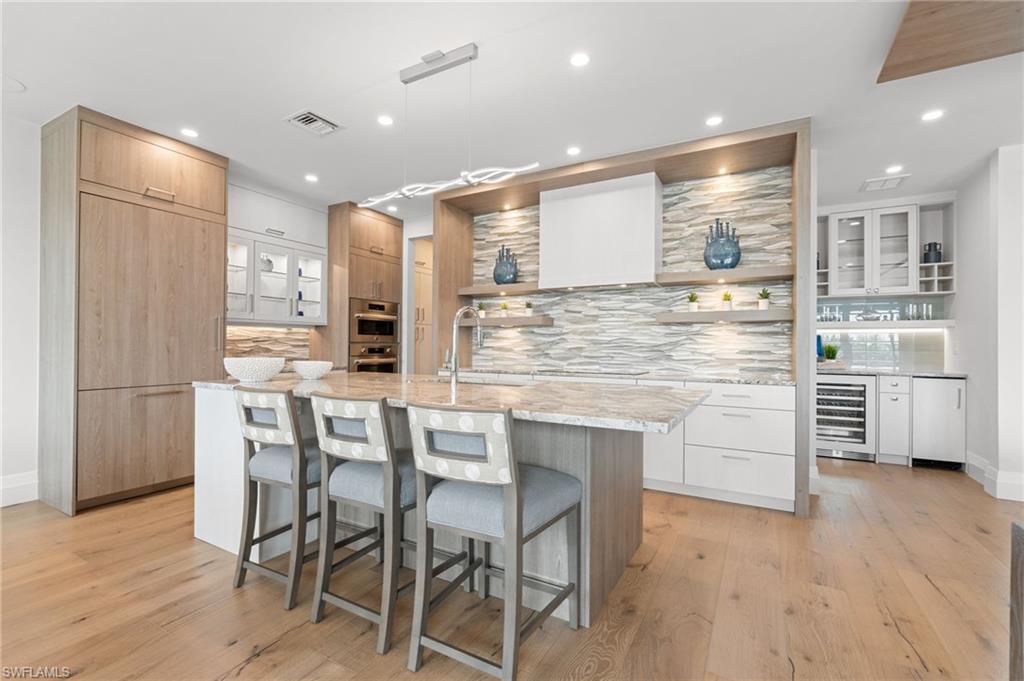 Kitchen featuring modern cabinets, open shelves, backsplash, light stone countertops, and glass insert cabinets