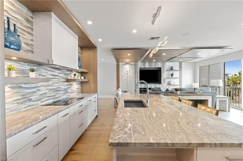 Kitchen with open shelves, a large island, light stone countertops, white cabinets, and modern cabinets