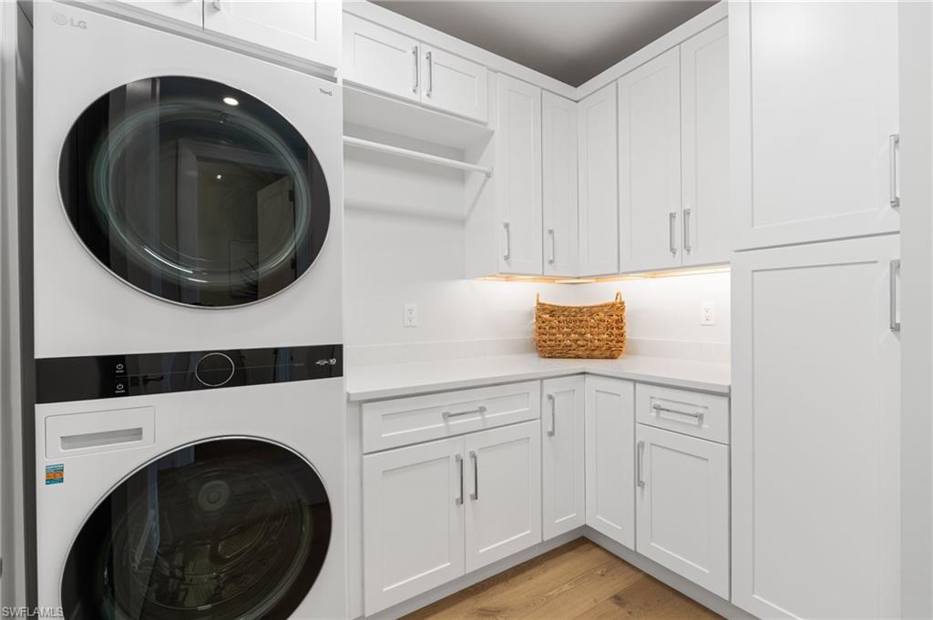 Laundry room featuring cabinet space, stacked washer / drying machine, and light wood-style flooring