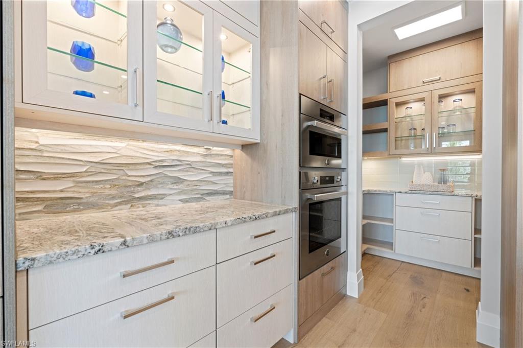 Kitchen featuring glass insert cabinets, light stone countertops, double oven, and modern cabinets