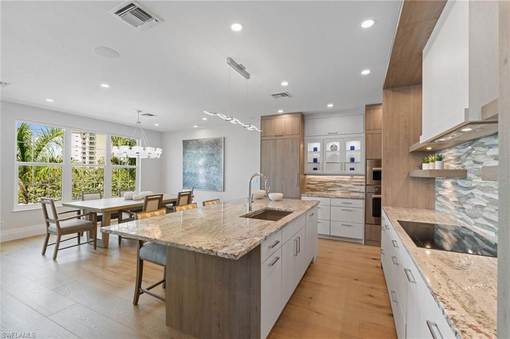 Kitchen with light stone counters, hanging light fixtures, light wood-type flooring, white cabinets, and backsplash