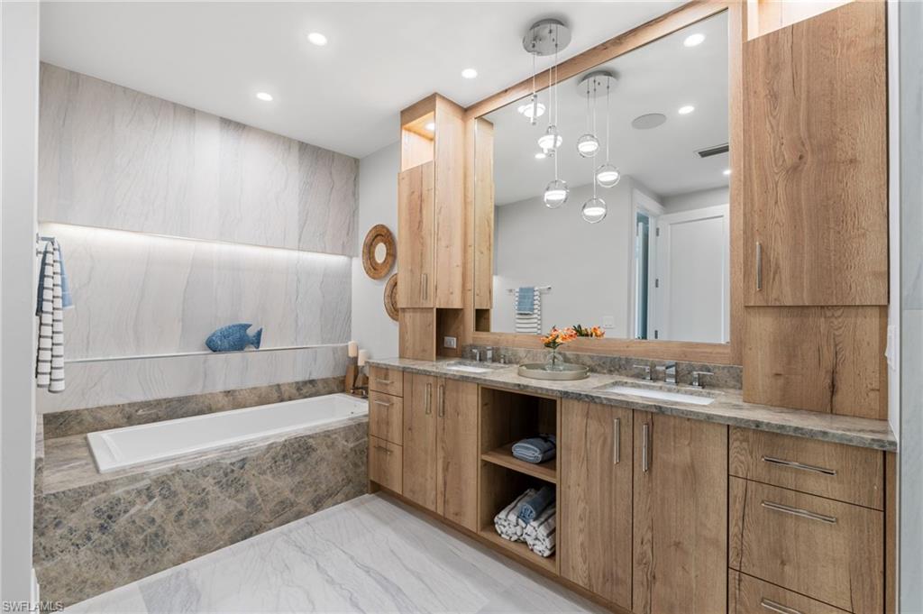 Full bathroom featuring double vanity, a bath, light marble finish floors, and recessed lighting