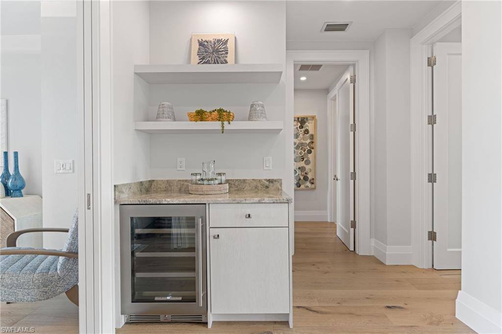 Indoor dry bar with wine cooler, light wood finished floors, open shelves, light stone counters, and white cabinetry