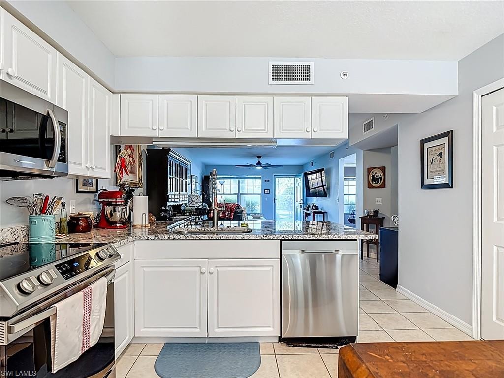 Kitchen featuring stainless steel appliances, white cabinets, light tile patterned flooring, and light stone countertops