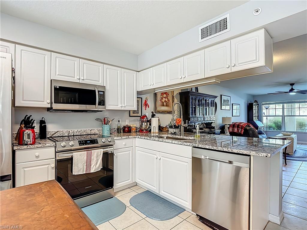 Kitchen with white cabinets, appliances with stainless steel finishes, light stone counters, ceiling fan, and light tile patterned floors