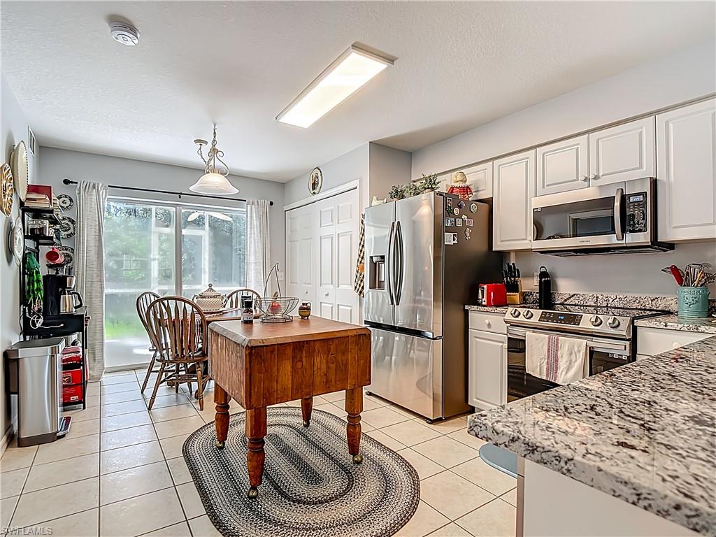 Kitchen featuring stainless steel appliances, light stone countertops, light tile patterned flooring, white cabinets, and a textured ceiling