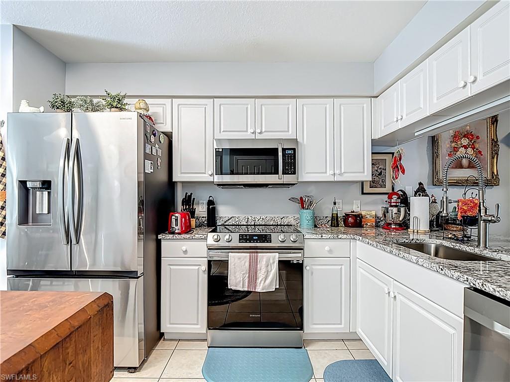 Kitchen featuring stainless steel appliances, light stone counters, white cabinetry, and light tile patterned floors