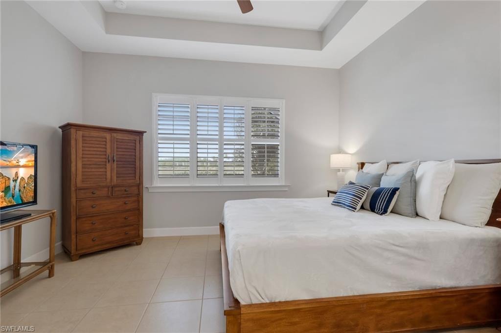 Bedroom with a raised ceiling, light tile patterned floors, and ceiling fan