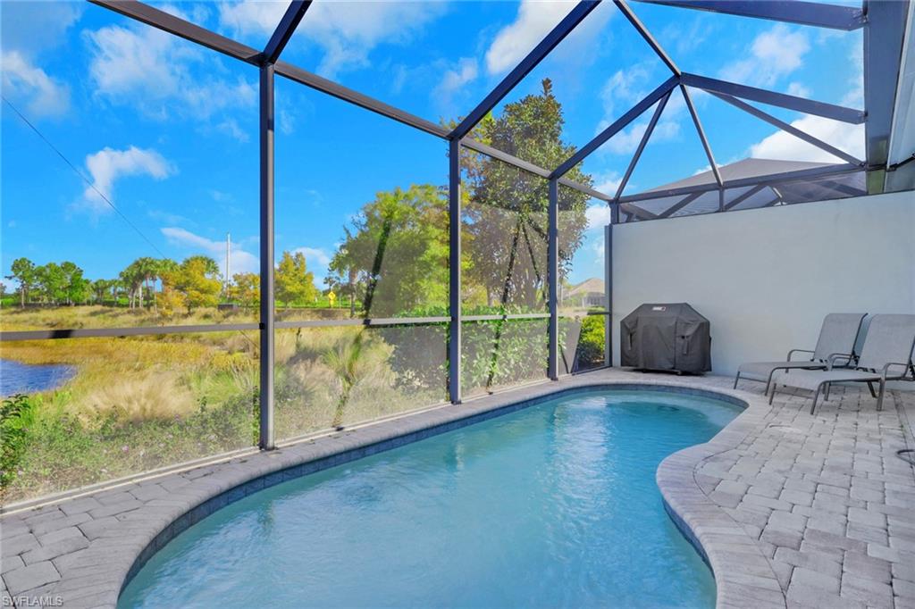 Outdoor pool with a sunroom, glass enclosure, area for grilling, a patio area, and a water view