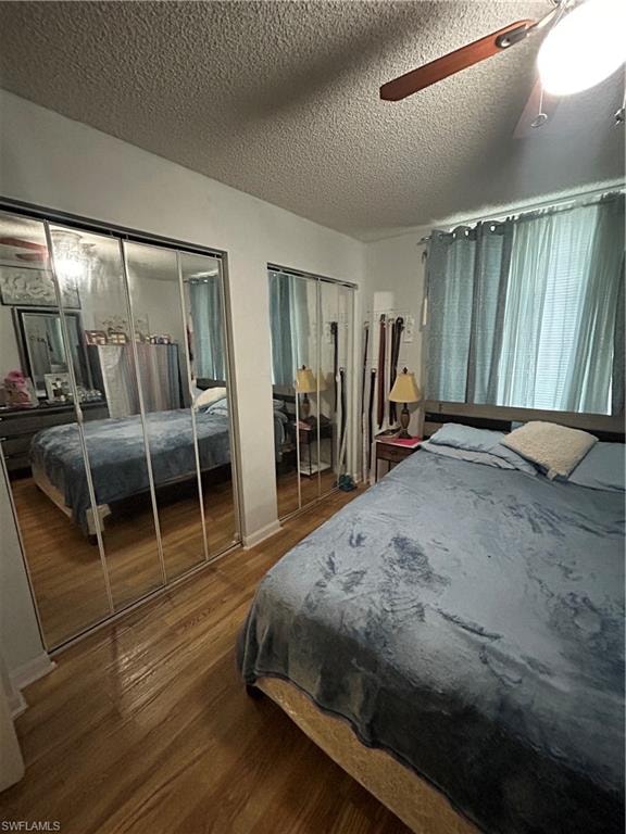 Bedroom with multiple closets, a textured ceiling, wood finished floors, and a ceiling fan